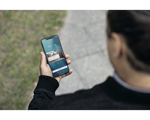 Eine Person hält ein Smartphone mit der Anzeige eines Wasseralarms in der Küche