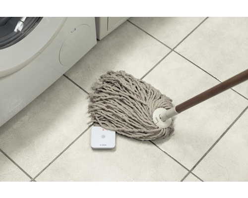 Ein Mopp liegt auf dem Boden neben einem Bosch Wassermelder in der Nähe einer Waschmaschine.