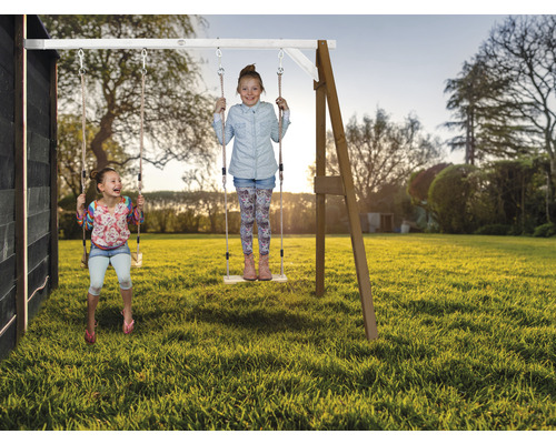 Zwei Kinder schwingen auf einer Holzschaukel im Garten.