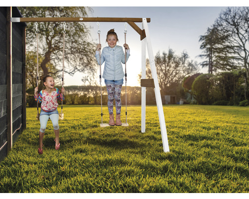 Zwei Kinder schwingen auf einer Holzschaukel im Garten.