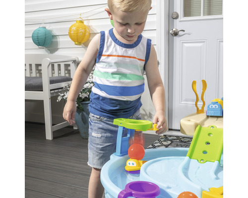 Kind spielt mit einem Outdoor-Wasserspieltisch auf einer Terrasse.