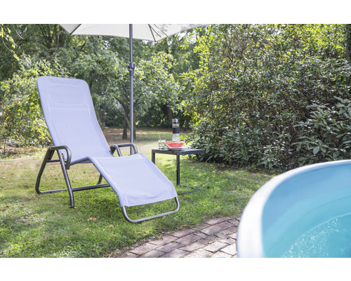 Gartenszene mit Liegestuhl, Sonnenschirm und kleinem Tisch auf einer Rasenfläche