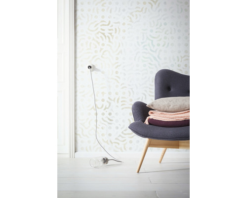 Szene mit gemusterter Tapete, Sessel mit Kissen und Dekorationen sowie einer Lampe auf dem Boden.