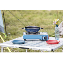 Campingtisch mit Gaskocher, Bratpfanne und Geschirr im Freien