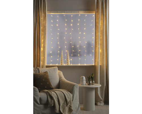Gemütliches Wohnzimmer mit Lichterketten, Vorhängen, Sessel und Beistelltisch für eine warme Atmosphäre.