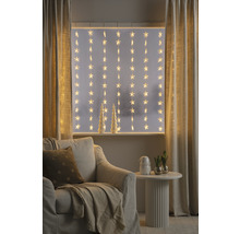 Dekoratives Wohnzimmer mit Sternenlichterkette vor dem Fenster, Sessel und Beistelltisch