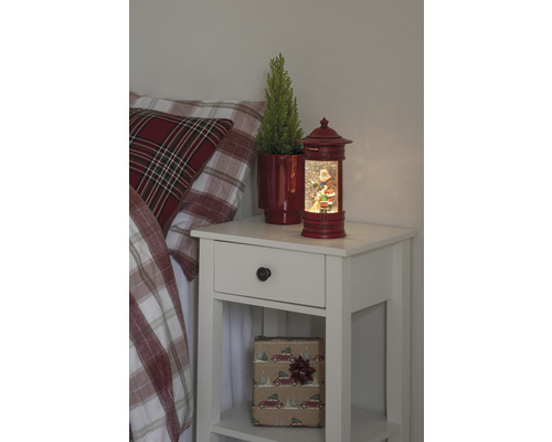 Nachttisch mit Weihnachtsdekoration, darunter eine Schneekugel mit Weihnachtsmannmotiv und eine Topfpflanze