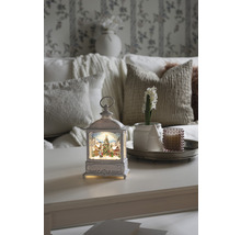 Dekorative Laterne mit Weihnachtsmotiv auf einem Tisch, umgeben von Wohnaccessoires für eine festliche Atmosphäre