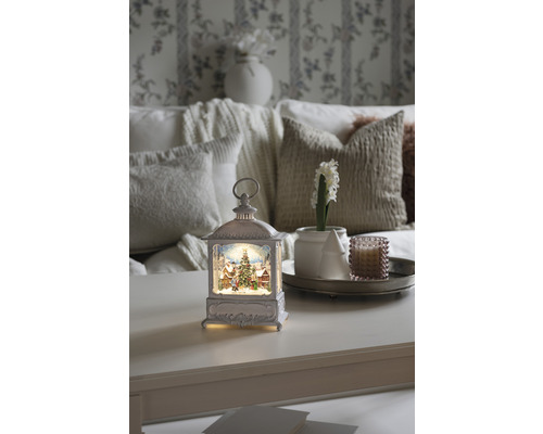 Dekorative Laterne mit Weihnachtsmotiv auf einem Tisch, umgeben von Wohnaccessoires für eine festliche Atmosphäre