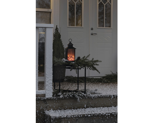 Dekorative Laterne mit Flammeneffekt auf einem Tisch vor einer Haustür im Winter.