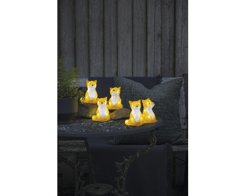Dekorative Fuchsfiguren auf einem Gartentisch mit Pflanze und Kissen