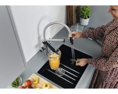 Eine Frau steht an einem Spültisch mit einem Wasserhahn und wäscht Kräuter.