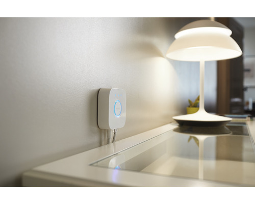 Philips Hue Bridge zur Steuerung von Smart Home Beleuchtung an der Wand montiert, neben einer Tischleuchte.