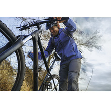 Mann schiebt ein schwarzes Mountainbike bergauf