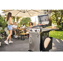 Gartenszene mit einem Gasgrill, einer Person, die Essen bringt, und einer Gruppe von Personen, die an einem Tisch sitzen
