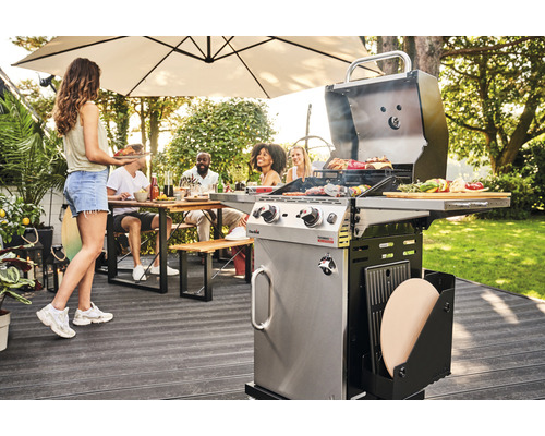 Gartenszene mit einem Gasgrill, einer Person, die Essen bringt, und einer Gruppe von Personen, die an einem Tisch sitzen