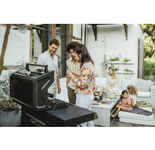 Eine Gruppe von Menschen steht um einen Grill bei einer Gartenparty.