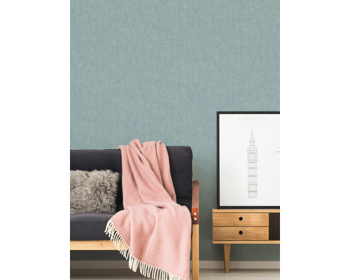 Wohnzimmer mit gemusterter Tapete, Sofa, Kissen, Decke und einem kleinen Schrank mit einem London-Bild