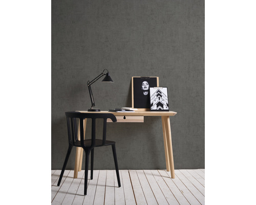 Schreibtisch mit Schublade, Schreibtischlampe und schwarzem Stuhl vor grauer Wand