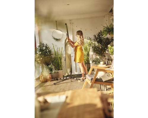 Frau bereitet eine Hängematte mit Gestell auf einem Balkon vor, umgeben von Pflanzen.