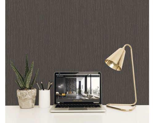 Nahaufnahme einer strukturierten, dunklen Tapete im Hintergrund eines Schreibtisches mit Laptop, Pflanze und Lampe