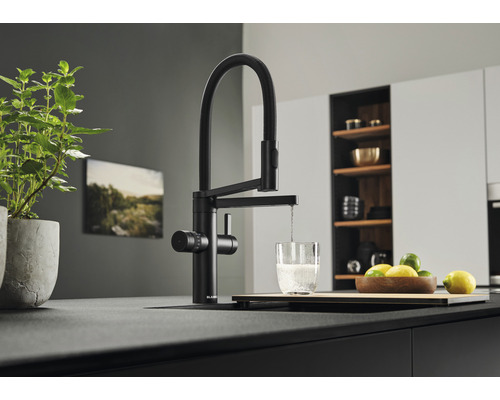 Küchenarmatur in Schwarz mit Wasserhahn, der Wasser in ein Glas fließen lässt, auf einer Arbeitsplatte in einer modernen Küche