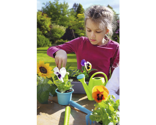 Mädchen pflanzt Blumen im Garten mit Gießkanne und Gartengeräten