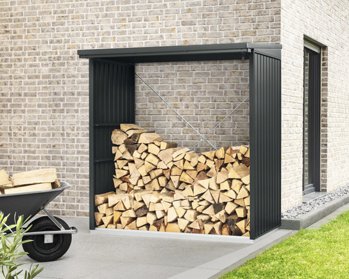 Brennholzlager mit Holz und Schubkarre vor einer Hauswand.