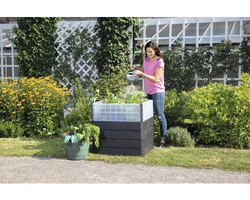 Frau gießt Pflanzen in einem Hochbeet aus Kunststoff im Garten.