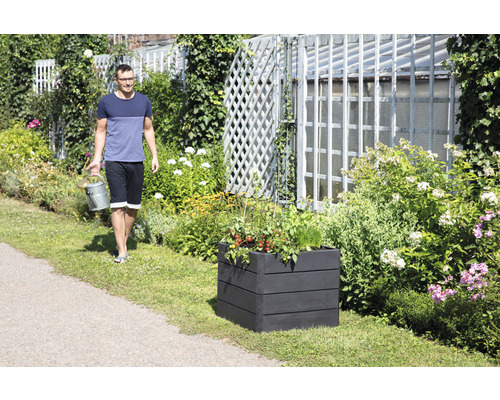 Mann mit Gießkanne neben einem bepflanzten Hochbeet im Garten.