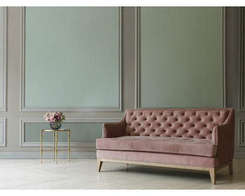 Gepolstertes Sofa mit Knopfheftung neben einem Beistelltisch mit Blumenstrauß vor einer verzierten Wand