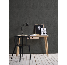Ein Arbeitszimmer mit Schreibtisch, Stuhl, Lampe und Dekoration vor einer dunklen Tapete.