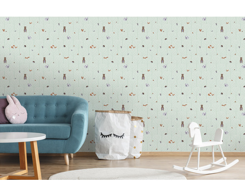 Kinderzimmer mit einer Tapete mit Waldtiermotiven, einem türkisfarbenen Sofa, einem runden Tisch und einem Schaukelpferd.