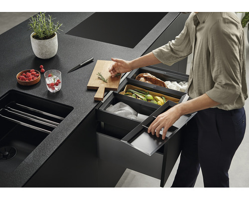 Küchenszene mit Mülleimern zur Abfalltrennung, Spüle, Schneidebrett, Messer, Schale mit Himbeeren und Pflanze im Topf