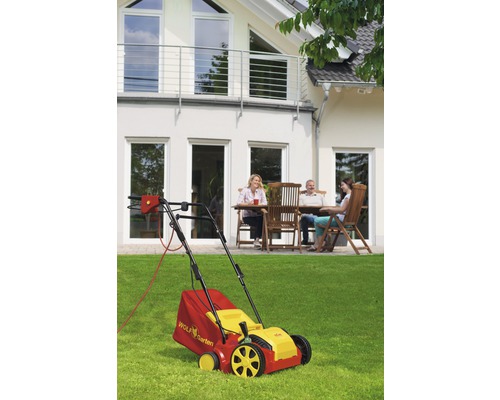 Szene mit einem Wolf Garten Rasenlüfter vor einem Haus mit Personen auf der Terrasse.