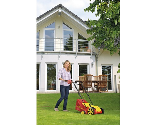 Frau benutzt einen elektrischen Rasenmäher der Marke Wolf Garten vor einem Haus.