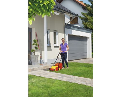 Frau bedient Rasenmäher im Garten vor dem Haus.