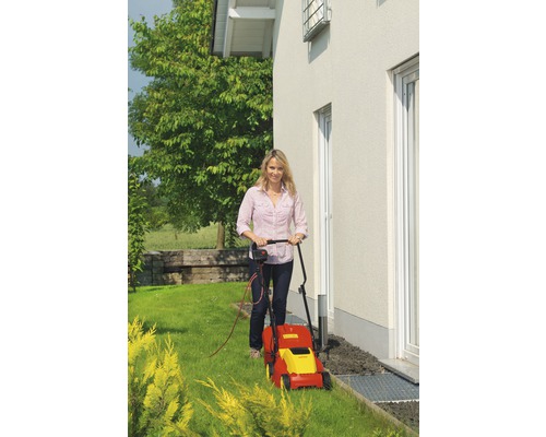 Frau beim Rasenmähen mit einem elektrischen Rasenmäher im Garten