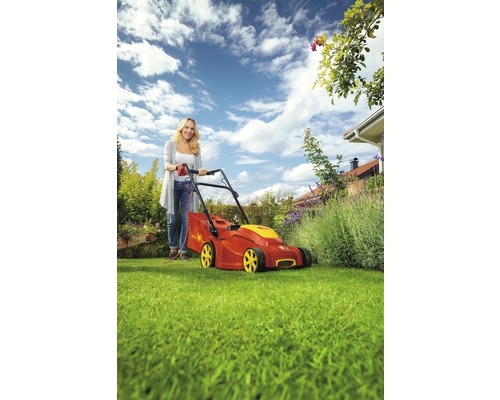 Frau bedient einen roten und gelben Rasenmäher auf Rasen