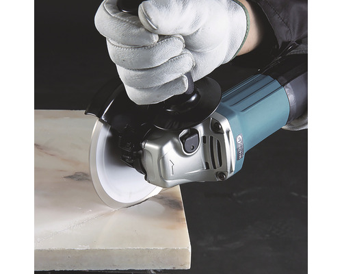 Ein Winkelschleifer mit Diamanttrennscheibe schneidet einen Stein, geschützt durch einen Handschuh.
