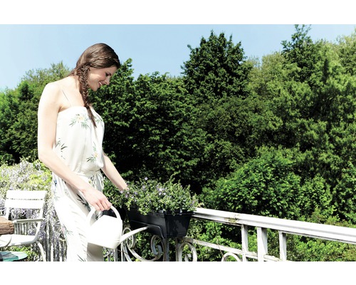 Frau gießt Blumen auf einem Balkon mit einer Gießkanne