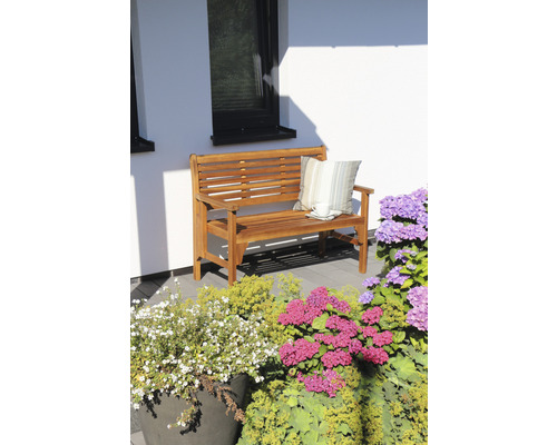 Holzbank mit Kissen und Tasse auf Terrasse neben Blumen