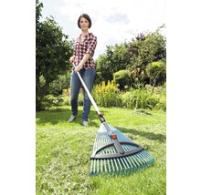 Eine Frau benutzt einen Laubbesen im Garten, um Gras zu rechen.
