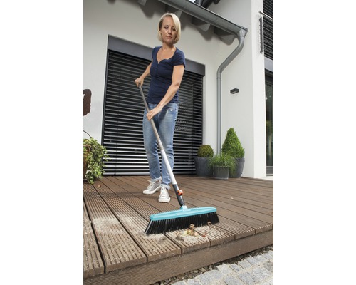Frau reinigt eine Holzterrasse mit einem Straßenbesen.