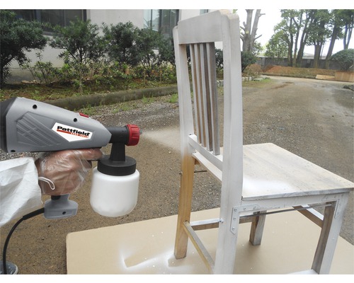 Farbsprühgerät beim Besprühen eines Holzstuhls