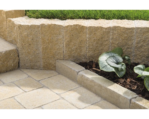 Detailansicht eines Gartens mit einer Mauer aus Pflanzsteinen, Rasenfläche und Bodenplatten.
