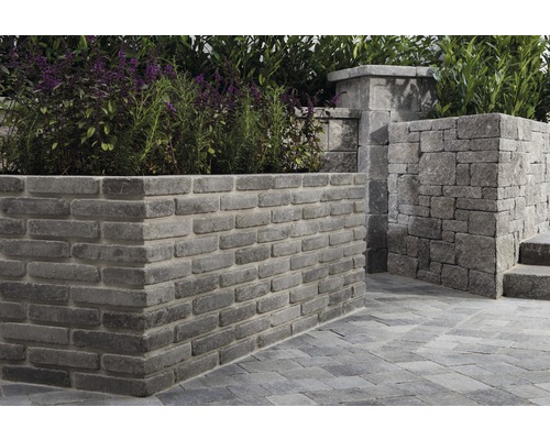 Garten mit einer Mauer aus grauen Pflastersteinen und blühenden Pflanzen