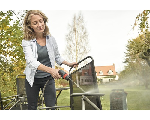 Frau reinigt Gartenstuhl mit Hochdruckreiniger im Garten