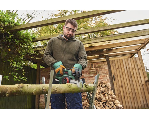 Mann sägt Holz mit einer Akku-Kettensäge im Garten