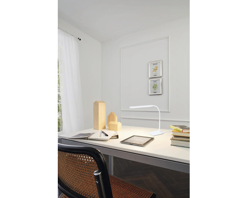 Schreibtisch mit Lampe, Notizbuch, Stift und Holzfiguren in einem hellen Zimmer.